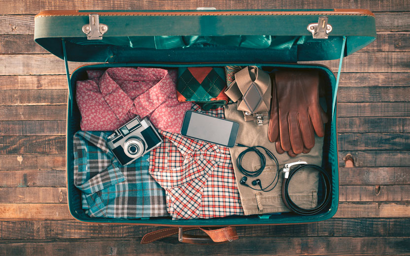 dicas para fazer a mala de viagem verde aberta, com camisas e acessórios dentro