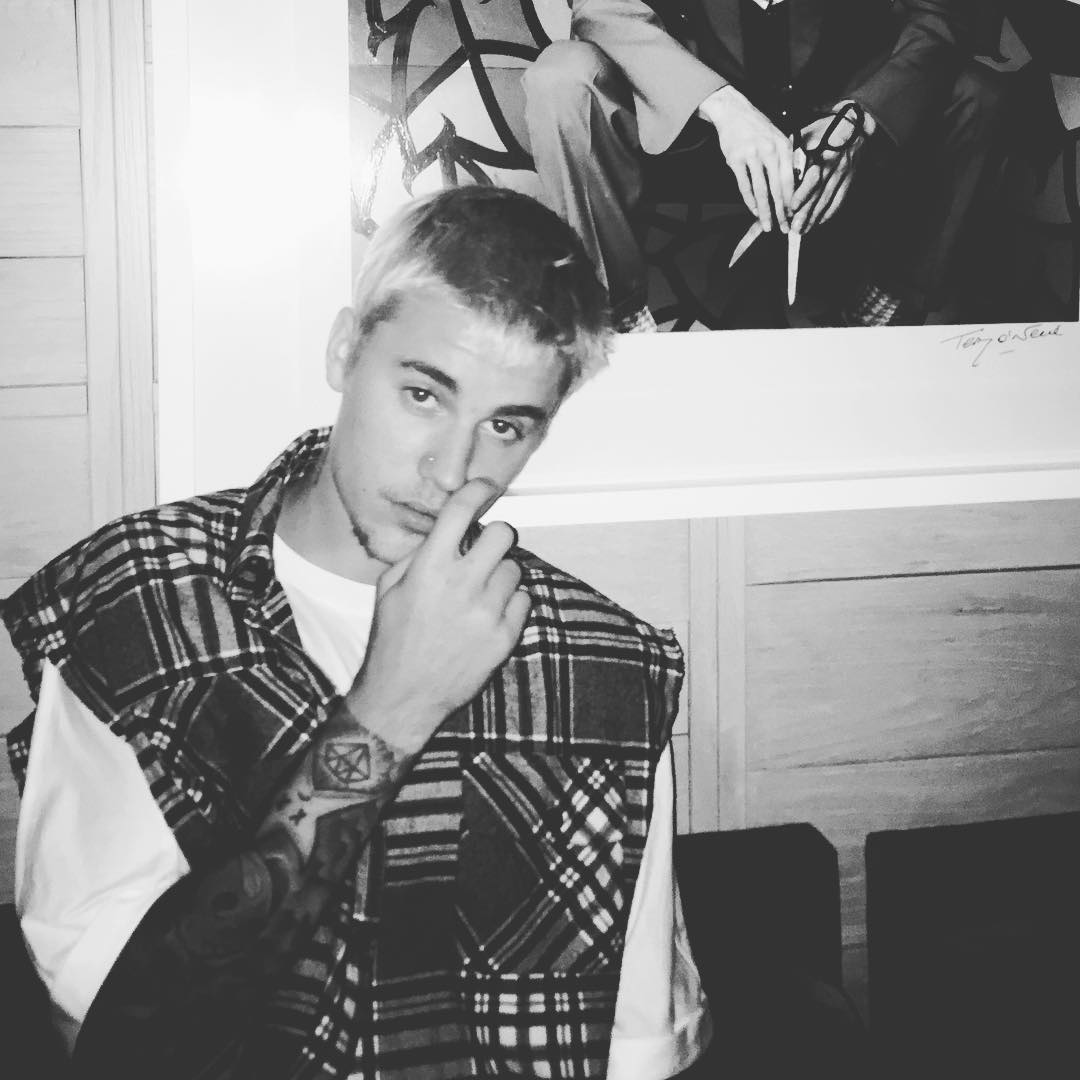 Justin Bieber em pé com a mão no rosto
