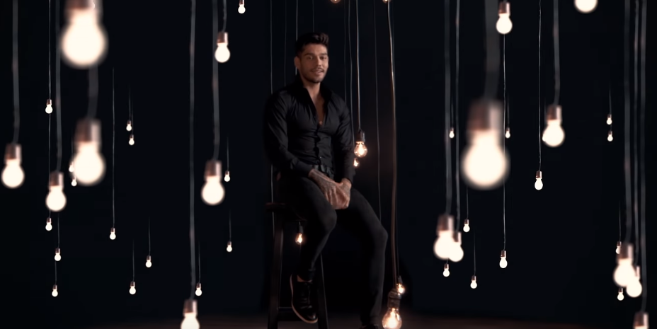Lucas Lucco no clipe de "Só não deixa eu tomar birra'' cercado de luzes em um fundo escuro