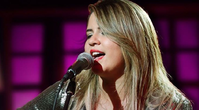 Marília Mendonça cantando em um fundo roxo