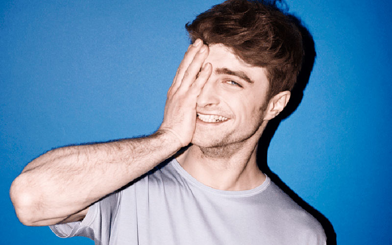daniel radcliffe com a mão no rosto em um fundo azul