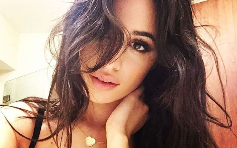 camila cabello com a mão no pescoço e com joia de coração