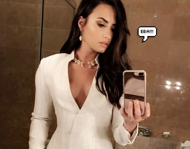 Demi Lovato com um celular na mão. Próximo à cabeça, há uma montagem de um balão escrito "eba!!!"