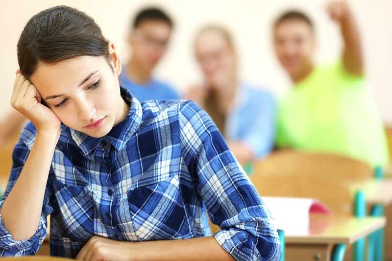 Menina de cabeça baixa no colégio sofrendo bullying de outros alunos