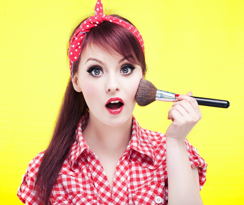 menina estilo pin-up passando um pincel nas bochechas