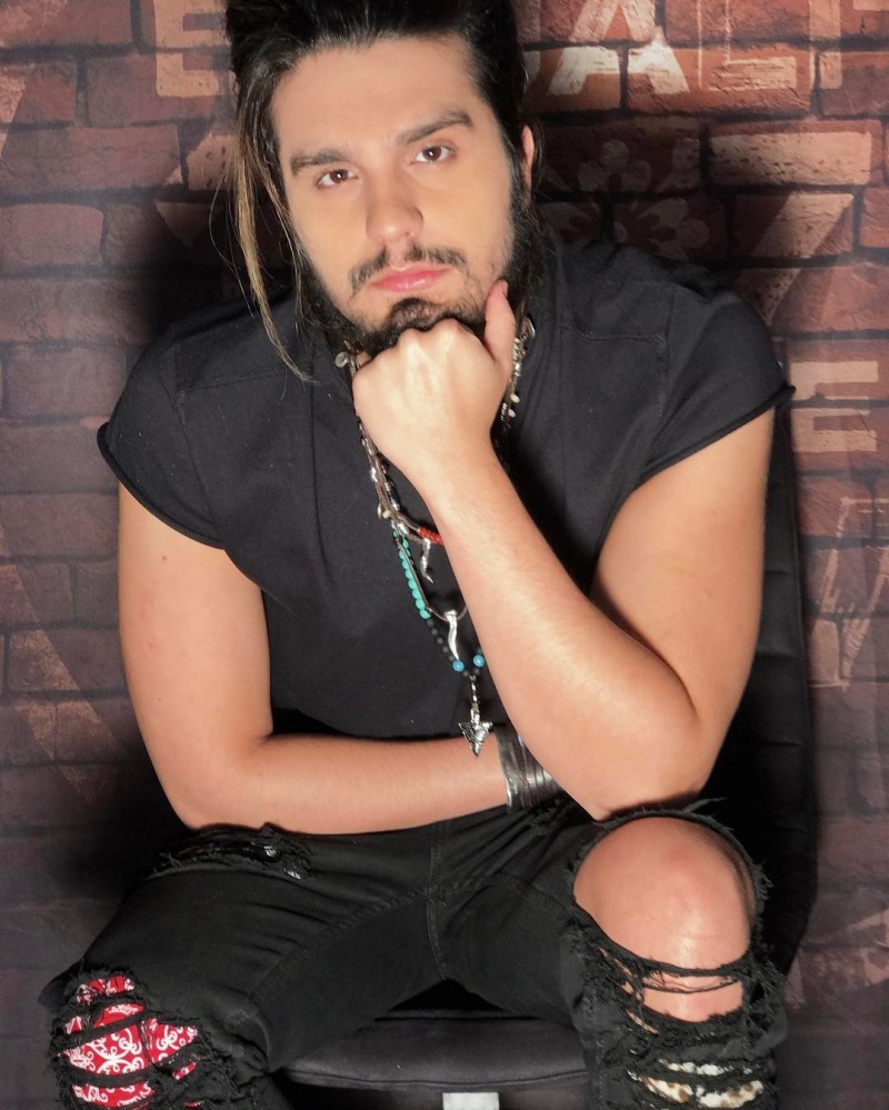 Luan Santana usa camiseta preta, olhando para a câmera e com a mão apoiando o rosto