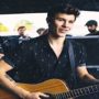 Shawn Mendes usando camisa estampada e tocando violão