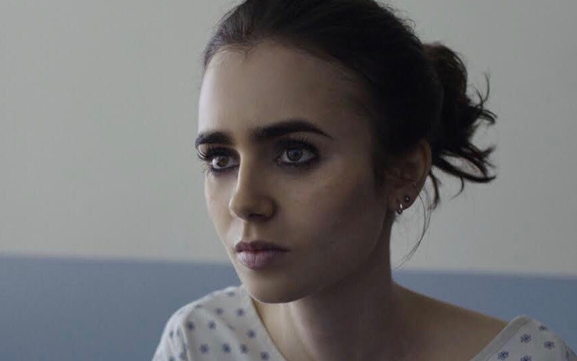 Lily Collins com os cabelos presos e usando avental de paciente de hospital