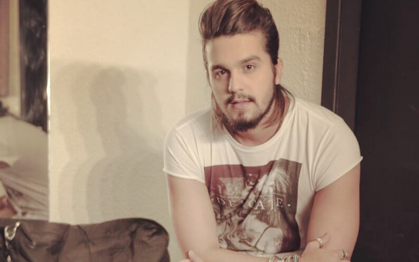 Luan Santana olha para câmera usando camiseta branca e de braços cruzados