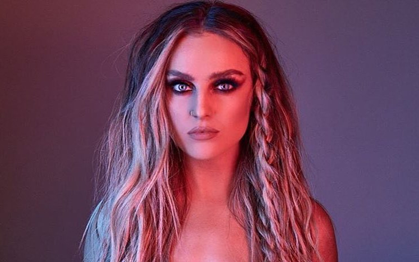 Perrie Edwards com os cabelos soltos, longos e loiros, em fundo roxo
