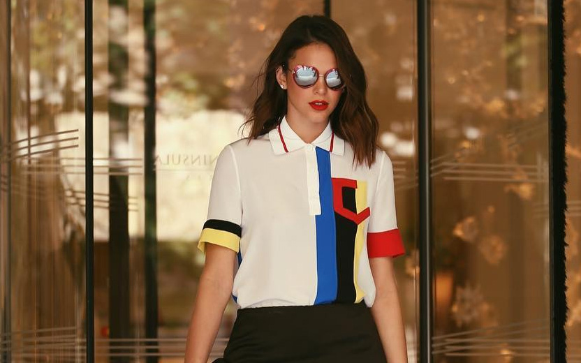 Bruna marquezine usa camisa branca com estampas em auzl, vermelho e amarelo, óculos e sol e sai de prédio com portas de vidro