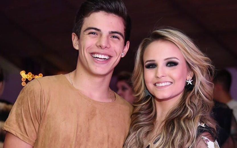 Larissa Manoela e Thomaz Costa: Thomaz Costa usa camiseta marrom e sorri ao lado de Larissa Manoela, que também sorri