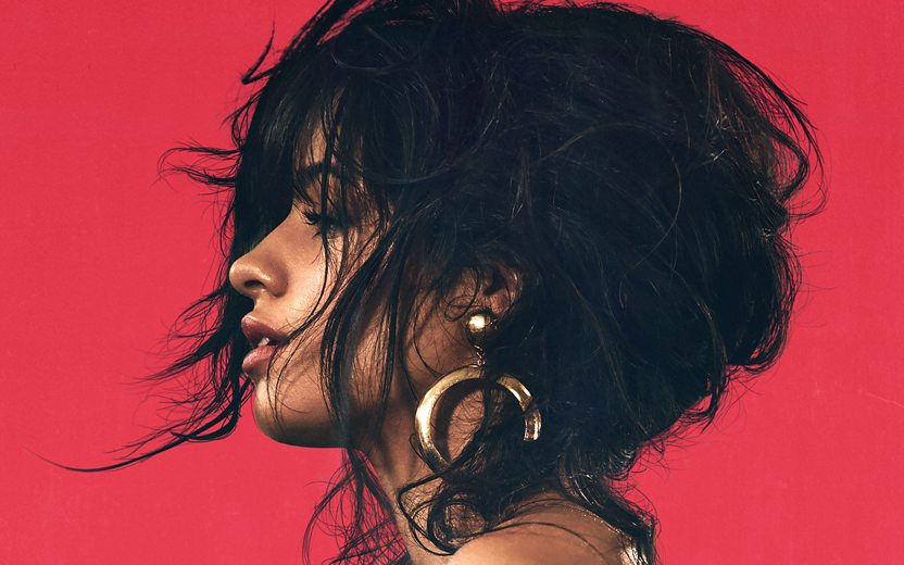 camila cabello de lado, com os cabelos presos e brinco dourado em fundo vermelho