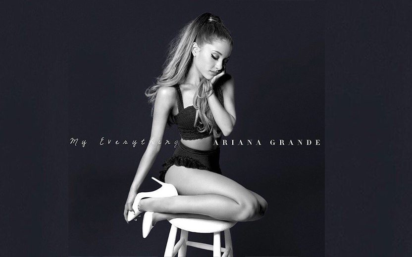 Ariana Grande em foto sentada em um banquinho com as pernas dobradas