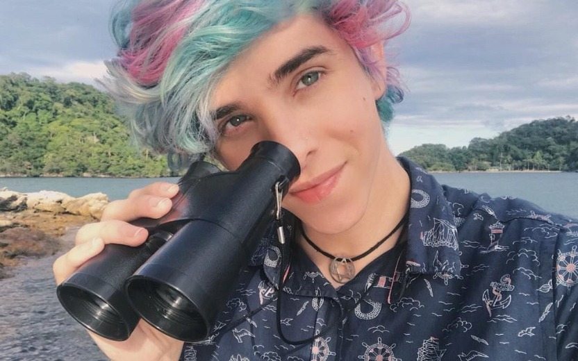 Erick Mafra, num close, segurando um binóculo e sorrindo