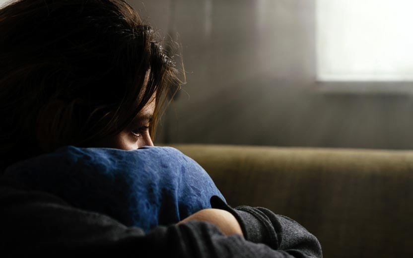 Suicídio na adolescência - Menina sentada segurando a perna com cara de sofrimento