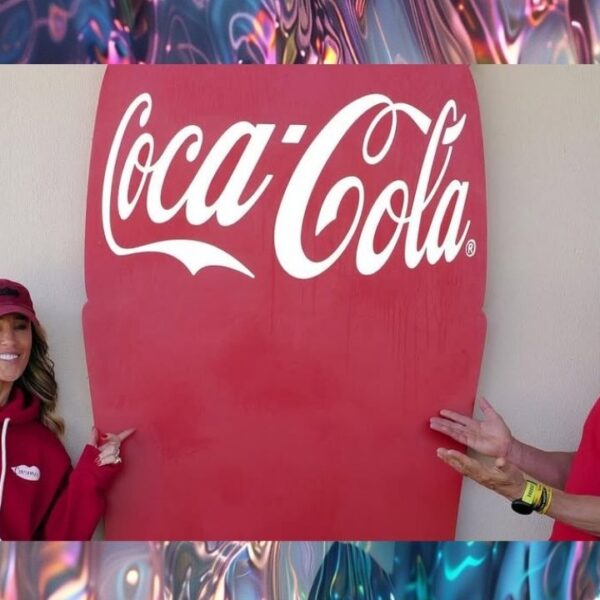 Karla e João Adibe Marques vestindo moletons vermelhos da Carmed posam sorridentes ao lado de uma grande placa com o logotipo da Coca-Cola.