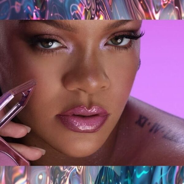 Close-up de Rihanna segurando um blush da Fenty Beauty, com maquiagem em tons de rosa e fundo lilás.